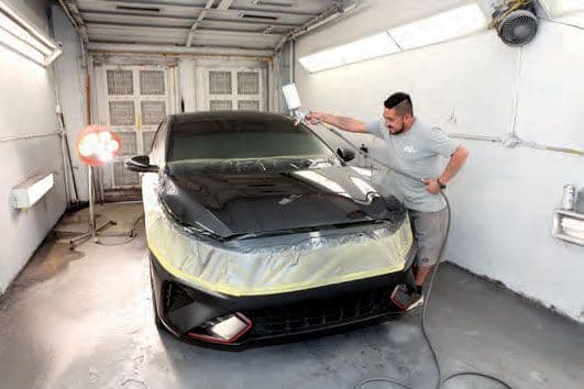 Painter spraying a masked black car inside the shop's paint booth
